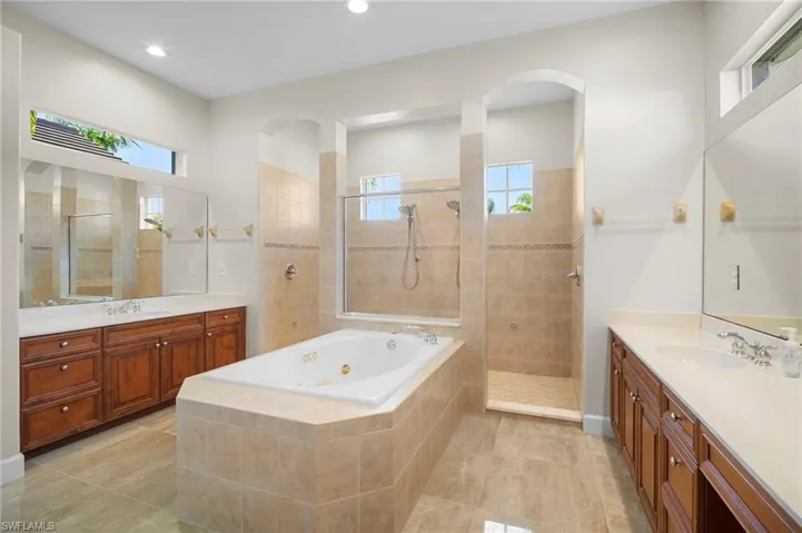 Bathroom featuring two vanities, a walk in shower, a jetted tub, and light tile patterned floors