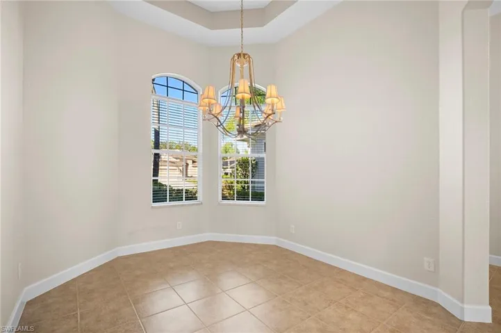 Empty room with a chandelier, a tray ceiling, and light tile patterned flooring
