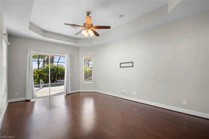 Empty room with a raised ceiling, a ceiling fan, and dark wood-type flooring