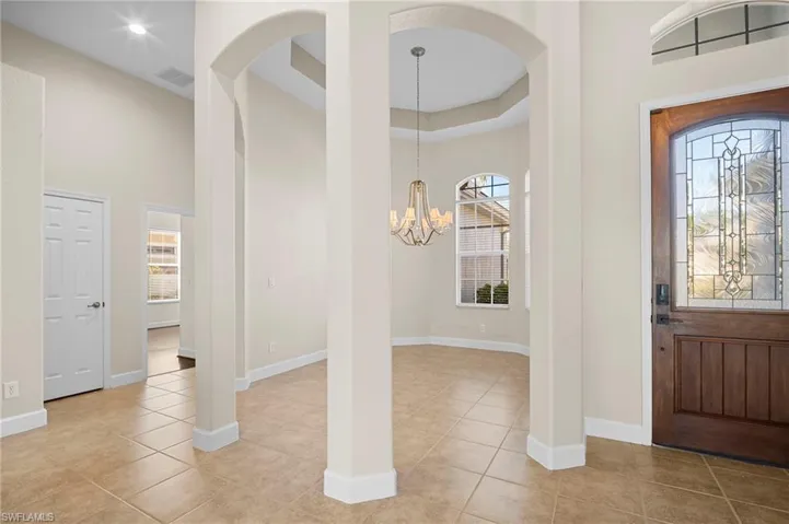 Entryway featuring healthy amount of natural light, a towering ceiling, a chandelier, light tile patterned floors, and arched walkways