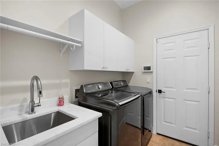 Washroom with cabinet space, washing machine and clothes dryer, light tile patterned floors, and a textured wall
