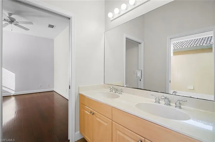 Full bathroom with double vanity, dark wood-style floors, healthy amount of natural light, and ceiling fan