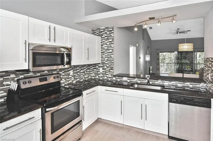 Kitchen featuring stainless steel appliances, lofted ceiling, backsplash, white cabinets, and a ceiling fan