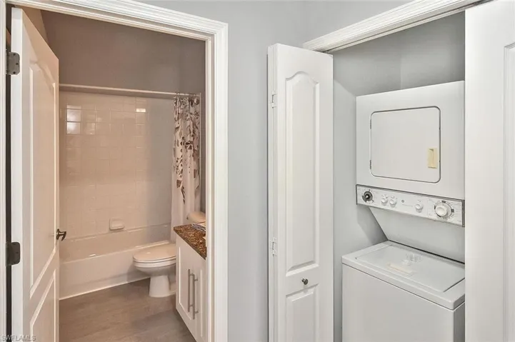 Laundry room featuring stacked washing machine and dryer and dark wood finished floors
