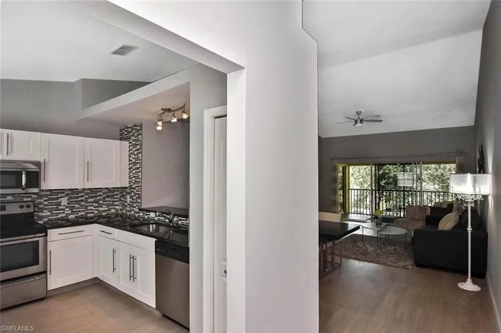 Kitchen featuring appliances with stainless steel finishes, wood finished floors, white cabinets, dark countertops, and backsplash