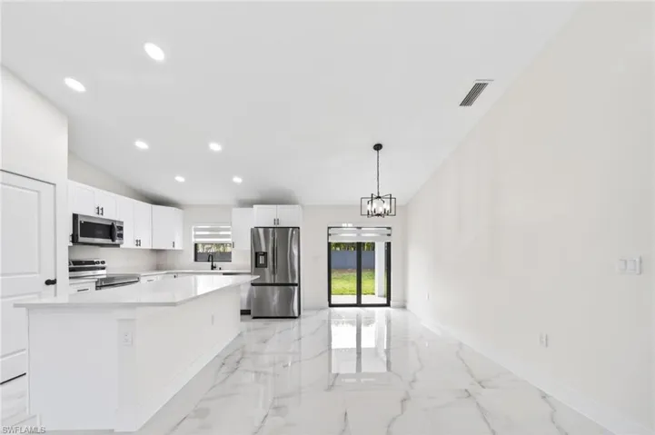 Open-concept living area featuring marble-look tile flooring, a vaulted ceiling with recessed lighting, and a modern kitchen