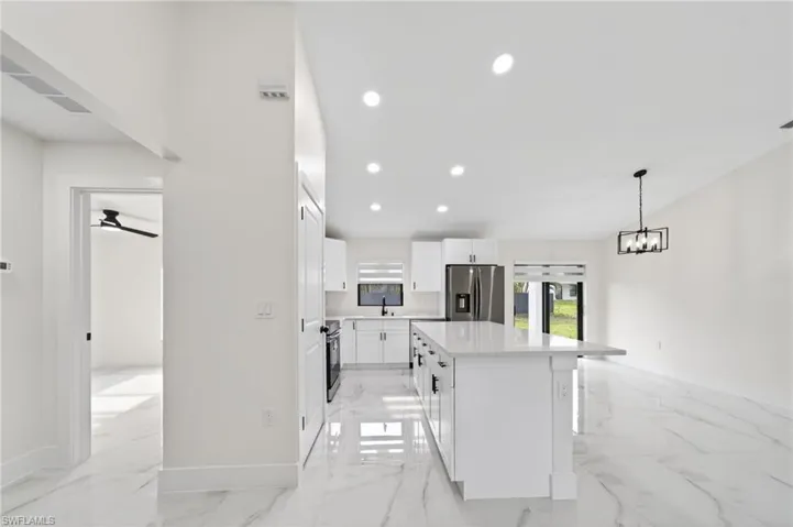 Open-concept kitchen and living area featuring white cabinetry, a large kitchen island with counter seating, stainless steel appliances, and white marble-look tile flooring