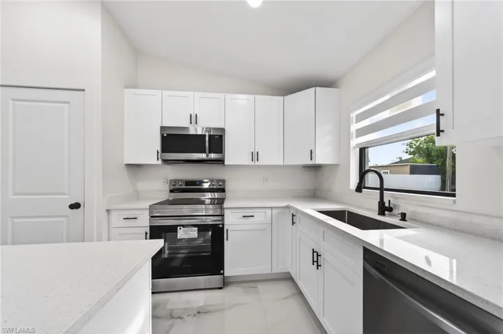 Modern kitchen featuring white shaker cabinetry, stainless steel appliances, light-toned countertops, a black sink with a coordinating faucet, and large format floor tile