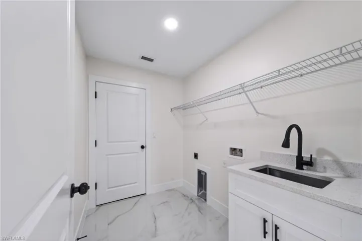 Laundry area featuring a built-in sink with a matte black faucet, light-toned countertop, and white cabinetry