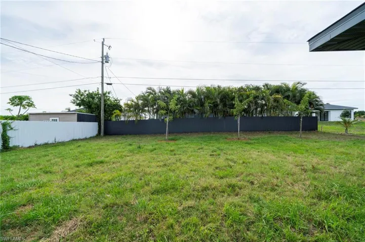 Expansive grassy yard area featuring a partial white picket fence and a dark privacy fence