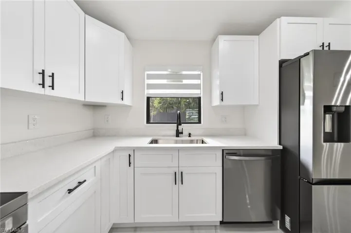 Modern kitchen featuring white shaker cabinetry, light-toned countertops, and a stainless steel sink with a black faucet