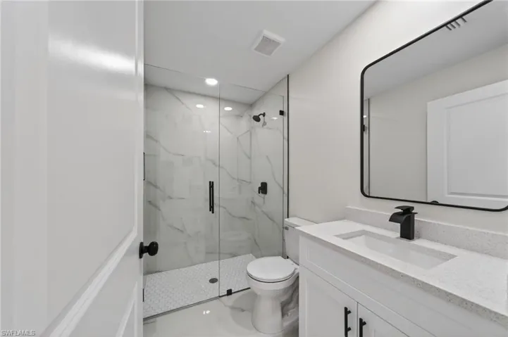 Bathroom featuring a frameless glass shower enclosure with white marble-look wall tiling and a hexagonal mosaic shower pan