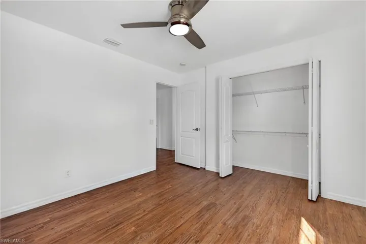 Spacious interior room featuring wood-finish flooring, a contemporary ceiling fan with integrated lighting, and a bi-fold closet with wire shelving