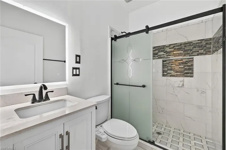 Modern bathroom featuring a white vanity with a light-toned countertop, an illuminated mirror, and matte black fixtures