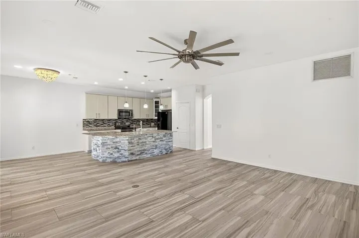 Open-concept interior featuring wood-finish tile flooring, a kitchen island with stacked stone detailing, stainless steel appliances, and pendant lighting