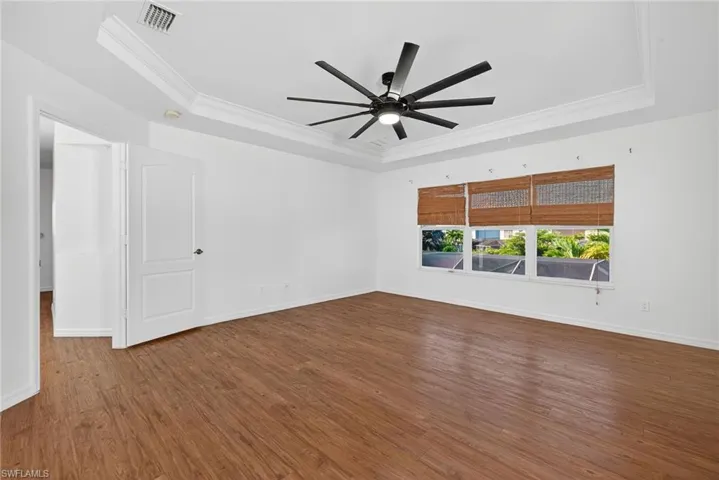 Spacious room featuring wood-finish flooring, a contemporary ceiling fan, and a tray ceiling with crown molding