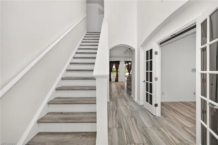 Foyer featuring a grand staircase with wood-finish treads and white risers, framed French doors, an arched entryway, and wood-look tile flooring