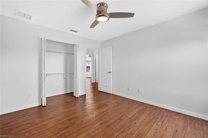 Spacious room featuring wood-finish flooring, light gray walls, a ceiling fan with integrated lighting, and a built-in closet with shelving
