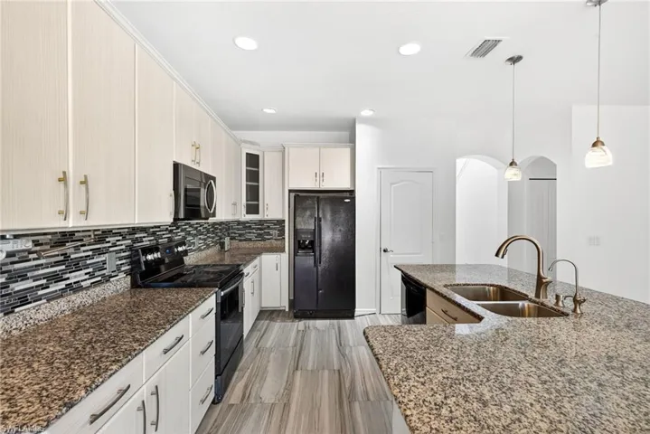 Kitchen featuring granite countertops, wood-finish flooring, a mosaic tile backsplash, stainless steel double basin sink, and pendant lighting
