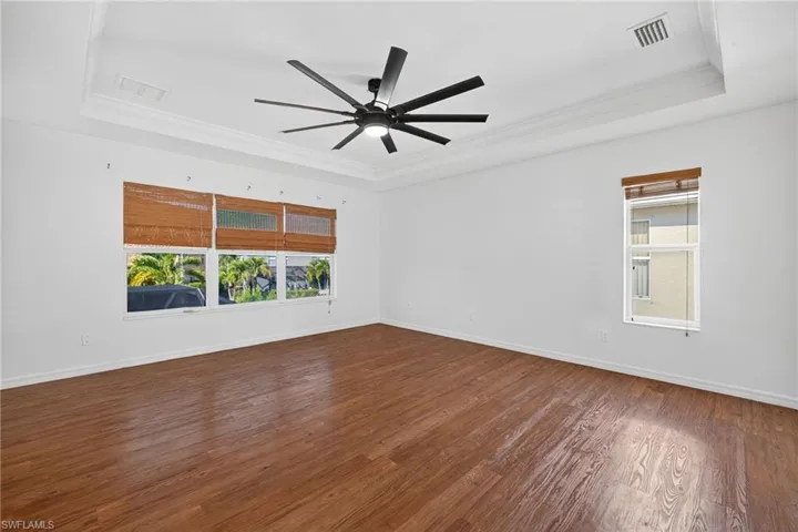Spacious room featuring a tray ceiling, contemporary ceiling fan, and wood-finish flooring
