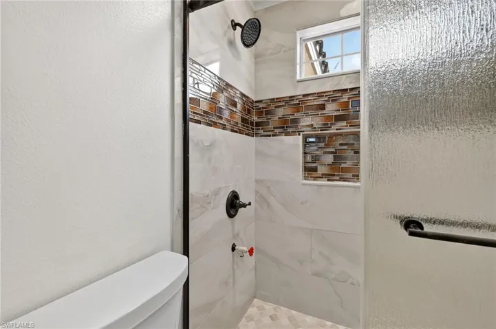 Walk-in shower featuring a mosaic tile accent band, integrated shower niche, and a tiled floor
