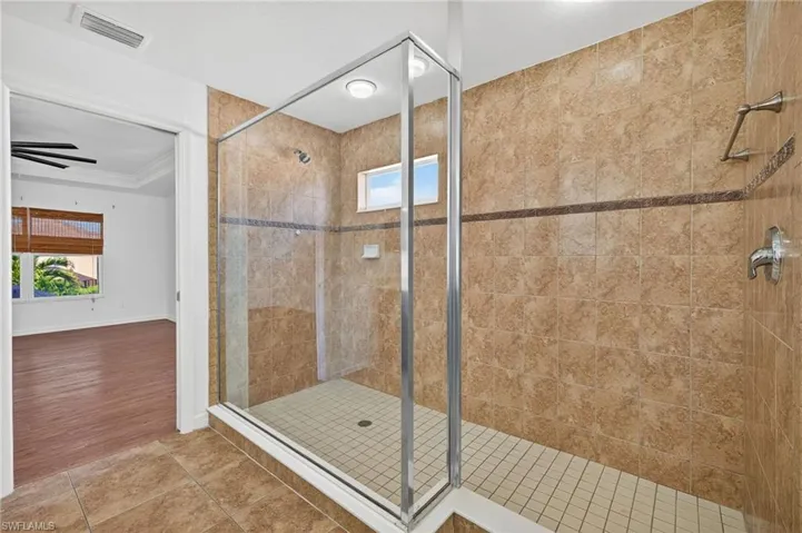 Spacious walk-in shower featuring glass enclosure, large format wall tiles with a decorative band, a small frosted window, and a square-tiled shower floor