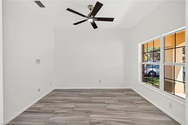 Spacious room featuring wood-finish flooring, a contemporary ceiling fan with integrated lighting, and multiple windows with grids
