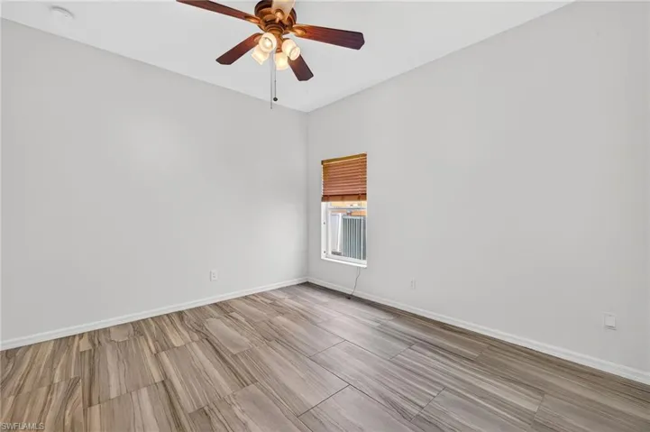 Room featuring wood-finish tile flooring, a window with wood blinds, a ceiling fan with light fixture, and white wall finishes