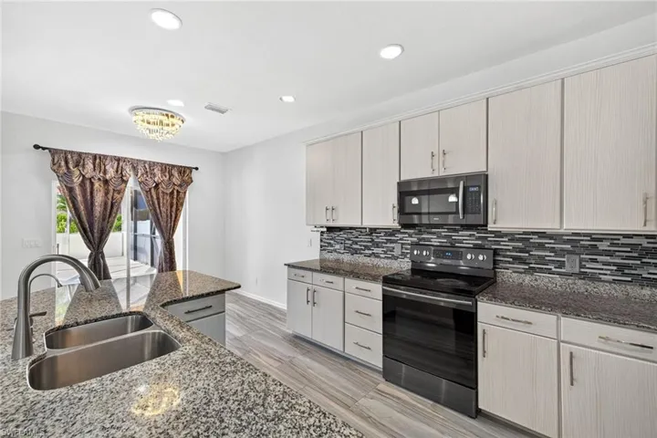 Modern kitchen featuring a double basin stainless steel sink, speckled countertops, light wood-finish cabinetry, a black electric range, and a coordinating microwave