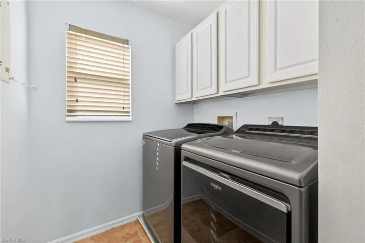 Laundry area featuring upper cabinetry, window with blinds, and tile flooring