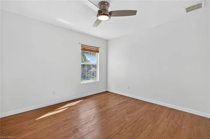 Room featuring wood-finish flooring, white baseboards, a window with a woven wood shade, and a ceiling fan with integrated lighting