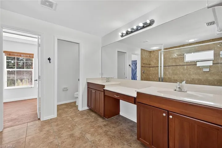 Bathroom featuring dual vanity with wood-finish cabinetry, light-toned countertops, and an integrated mirror