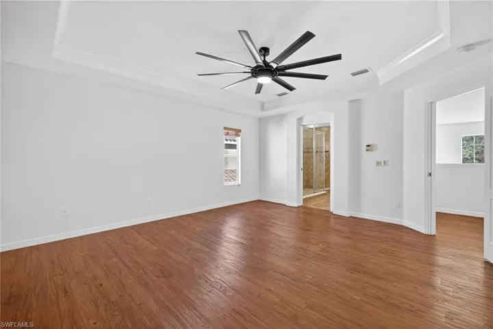 Spacious room featuring wood-finish flooring, a tray ceiling, and a contemporary ceiling fan