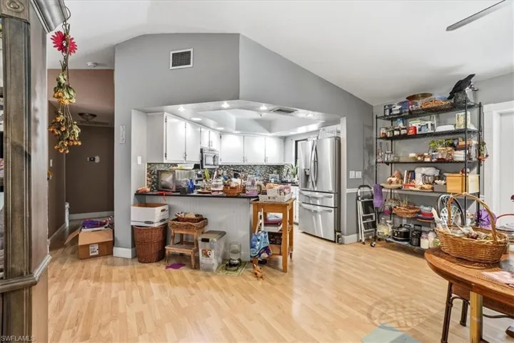 Kitchen with a peninsula, stainless steel appliances, white cabinetry, light wood-style flooring, and vaulted ceiling