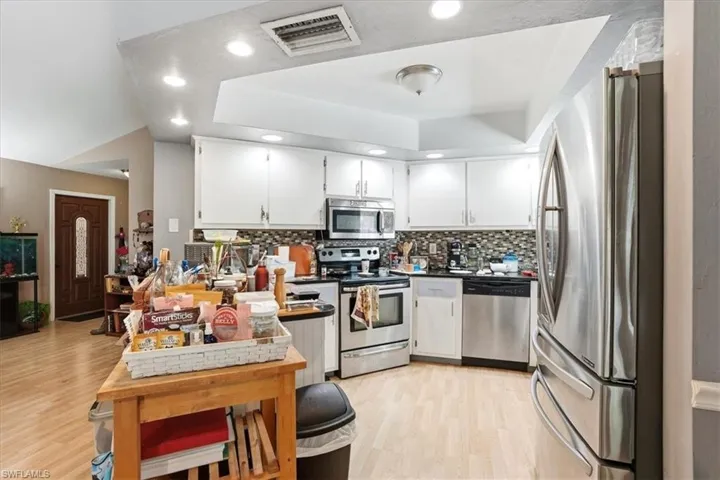 Kitchen featuring stainless steel appliances, light wood-style floors, white cabinets, backsplash, and dark countertops