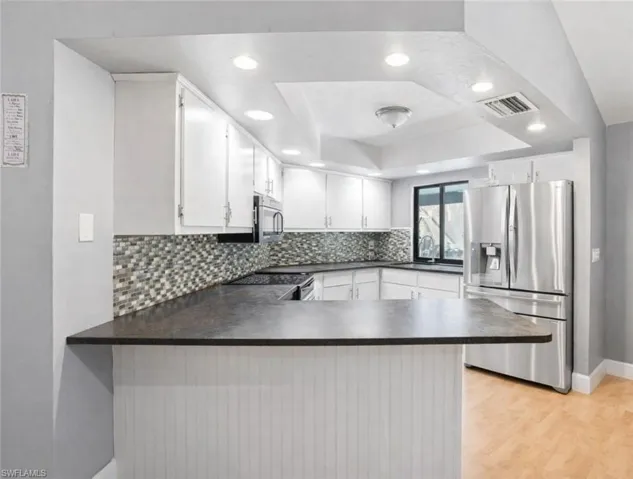 VIRTUALLY STAGED. Kitchen with stainless steel appliances, white cabinets, a peninsula, backsplash, and dark countertops