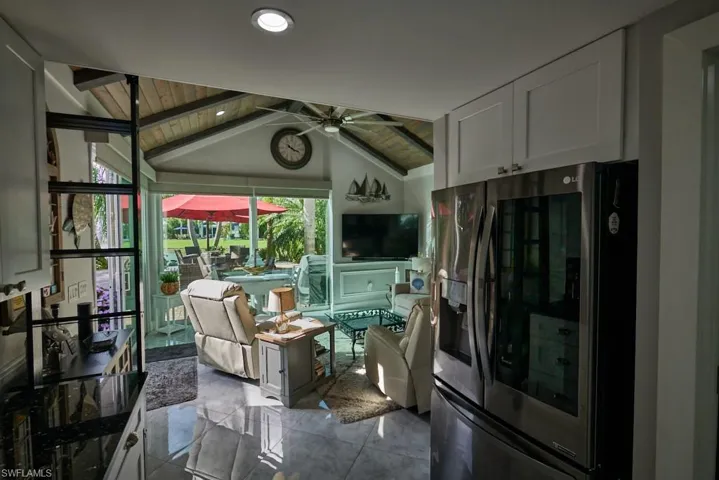 Kitchen featuring stainless steel refrigerator with ice dispenser, wood ceiling, white cabinets, ceiling fan, and vaulted ceiling with beams