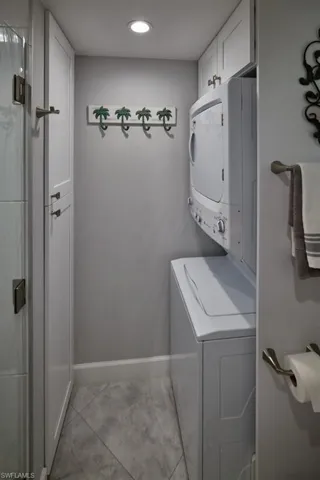Washroom with stacked washer and clothes dryer, cabinets, and light tile patterned floors