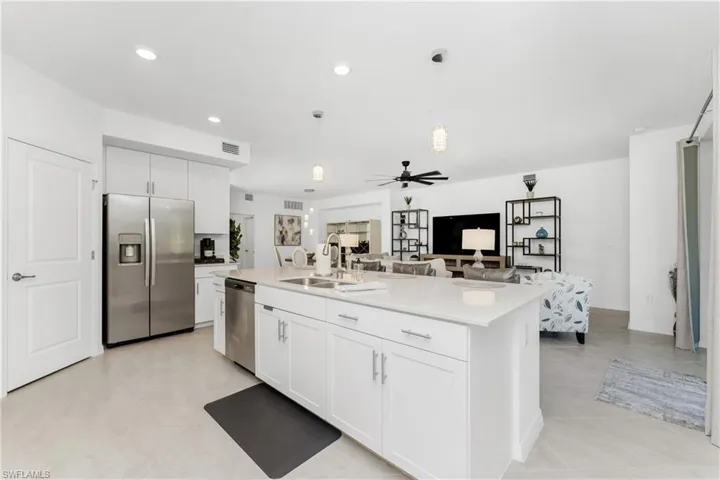 Kitchen featuring stainless steel appliances, white cabinetry, decorative light fixtures, open floor plan, and a center island with sink