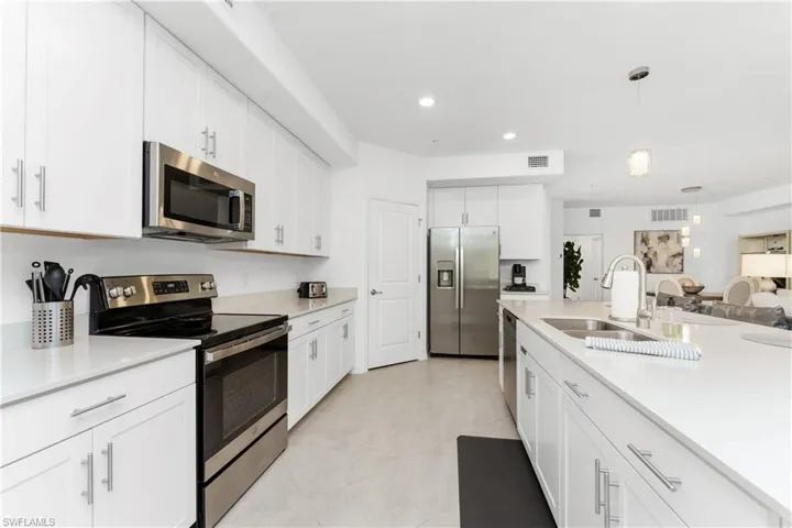 Kitchen with stainless steel appliances, white cabinetry, pendant lighting, light stone counters, and open floor plan