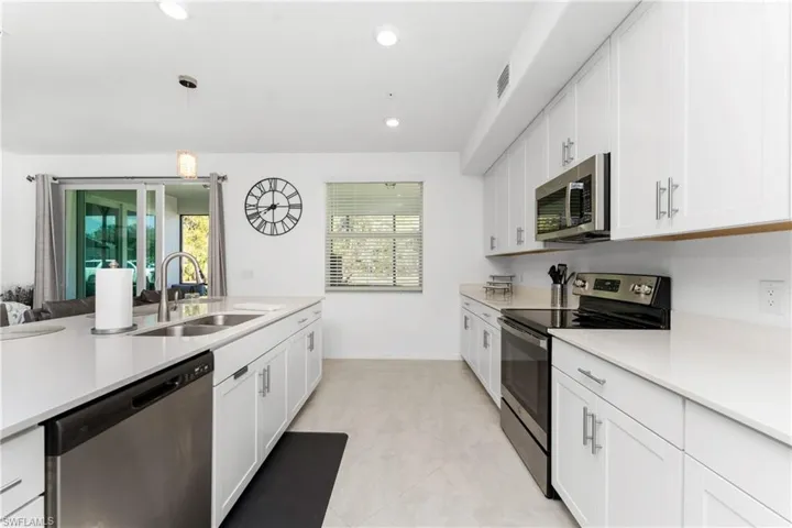Kitchen with stainless steel appliances, white cabinetry, hanging light fixtures, light stone counters, and light tile patterned flooring