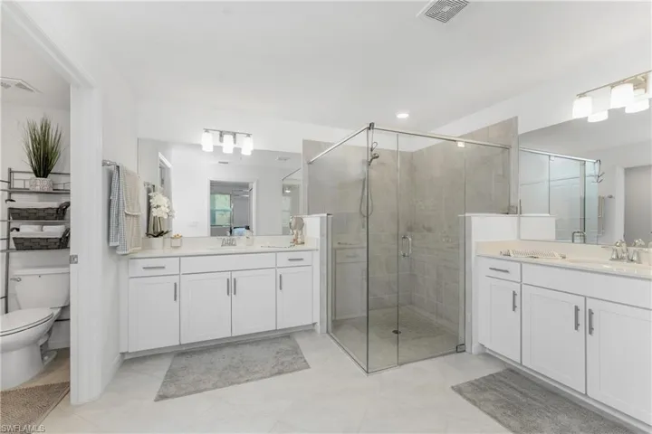 Bathroom featuring a shower stall, two vanities, and light tile patterned floors