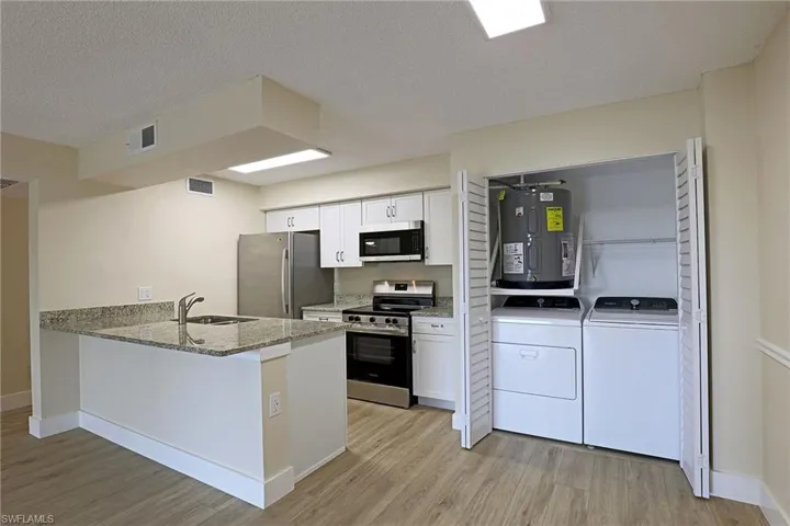 Kitchen featuring stainless steel appliances, light stone countertops, white cabinetry, light wood-style floors, and electric water heater