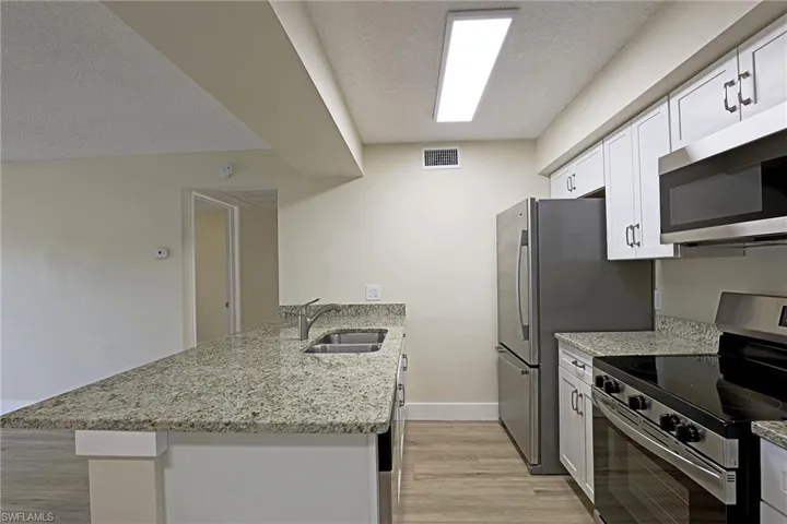 Kitchen featuring stainless steel appliances, a peninsula, light stone counters, a textured ceiling, and light wood-style floors