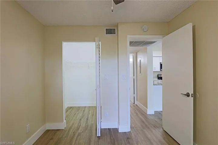 Unfurnished bedroom with a textured ceiling, light wood finished floors, a walk in closet, and a ceiling fan