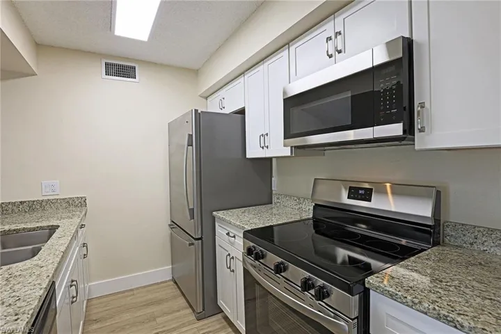 Kitchen featuring stainless steel appliances, light stone countertops, white cabinets, light wood-type flooring, and a textured ceiling
