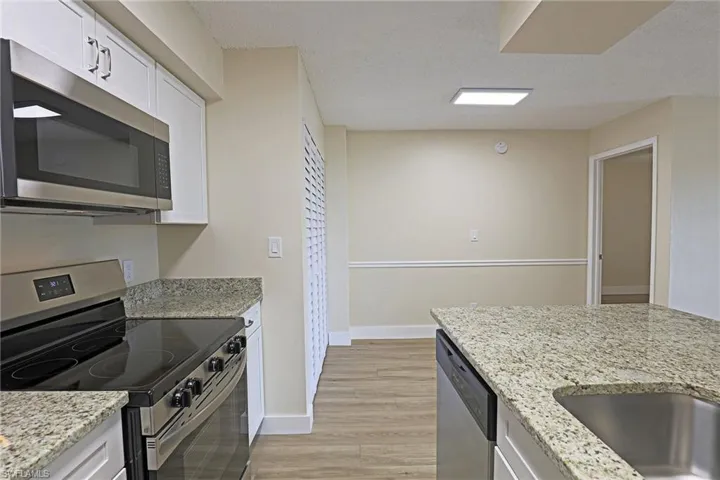 Kitchen with stainless steel appliances, white cabinetry, light stone countertops, and a textured ceiling