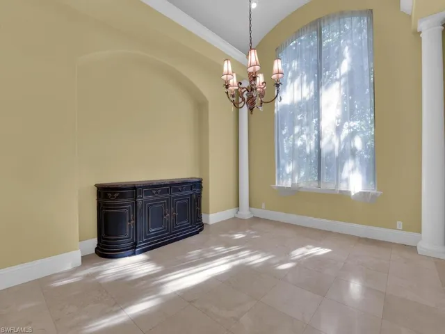 Empty room featuring decorative columns, a chandelier, and crown molding