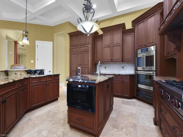 Kitchen featuring coffered ceiling, pendant lighting, appliances with stainless steel finishes, dark stone counters, and backsplash