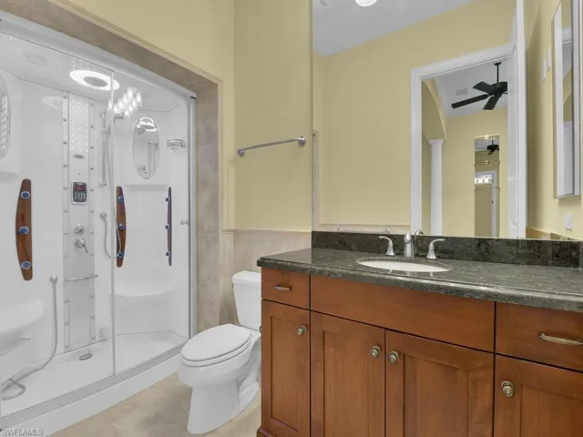 Full bath featuring vanity, a stall shower, a ceiling fan, and tile walls